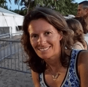 Smiling middle aged white women with shoulder length brown hair standing outside in a dark blue pattern tank top